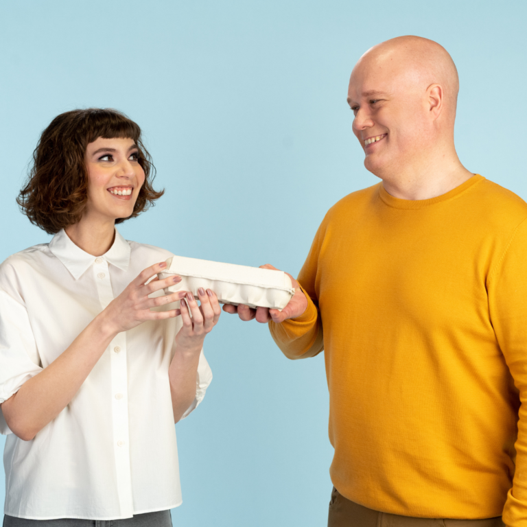 Kaksi hymyilevää kuluttajaa kartonkipakkaus kädessä